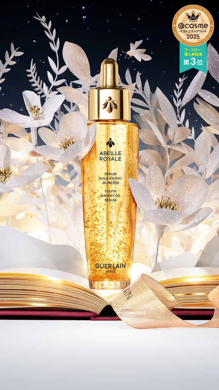Guerlain's Abeille Royale Youth Watery Oil serum bottle displayed on top of a book, set against a flowery night-blue background