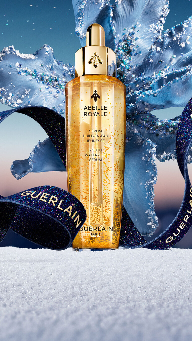 Abeille Royale Youth Watery Oil Serum Bottle with a Blue Sparkling Holiday Ribbon and snowy background